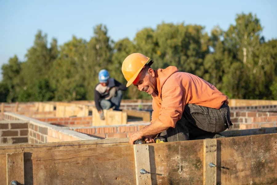 Un maçon casqué travaille sur un coffrage, au-dessus d'un mur de briques
