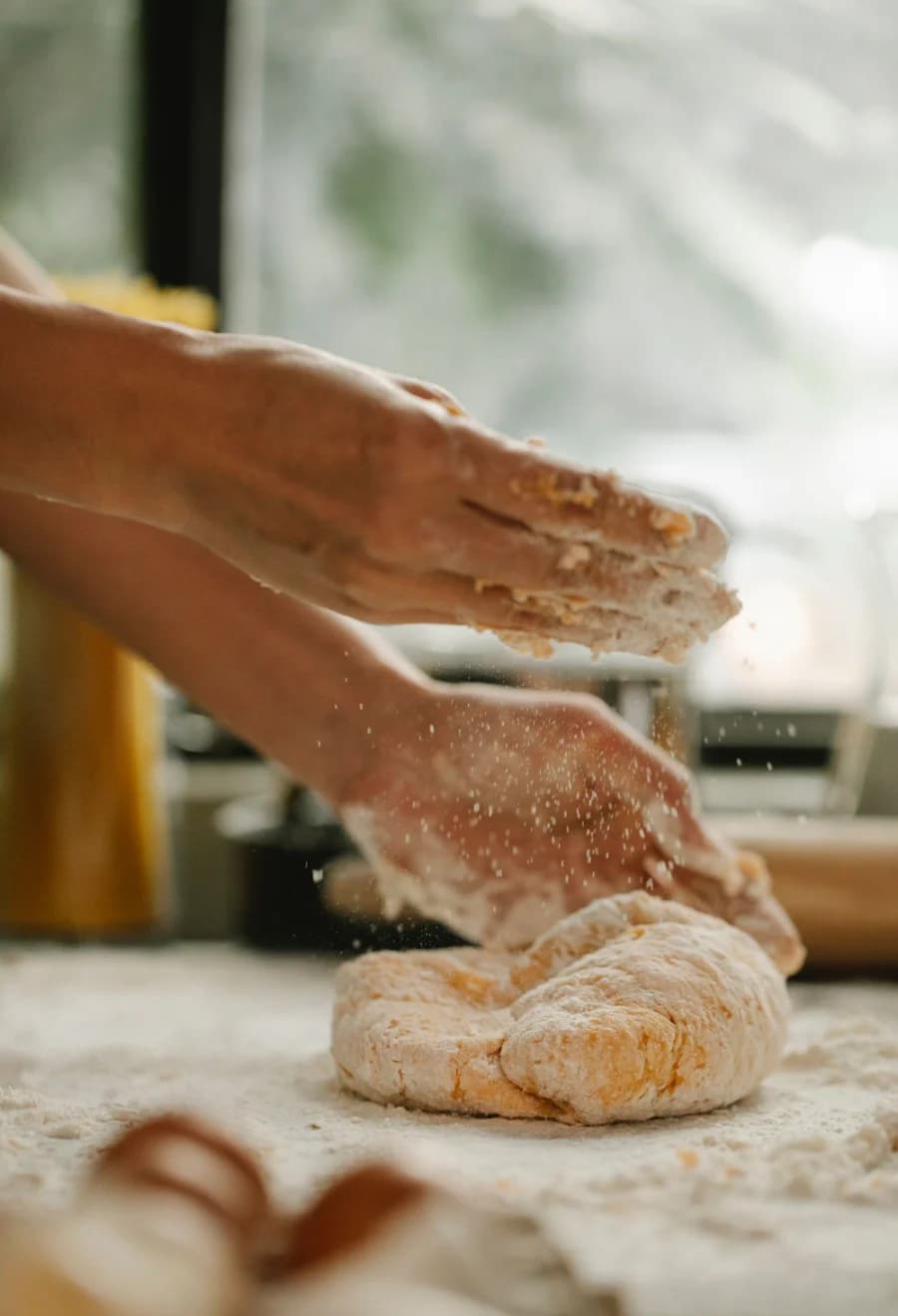 Deux mains farinées travaillent une pâte à pain sur un plan de travail