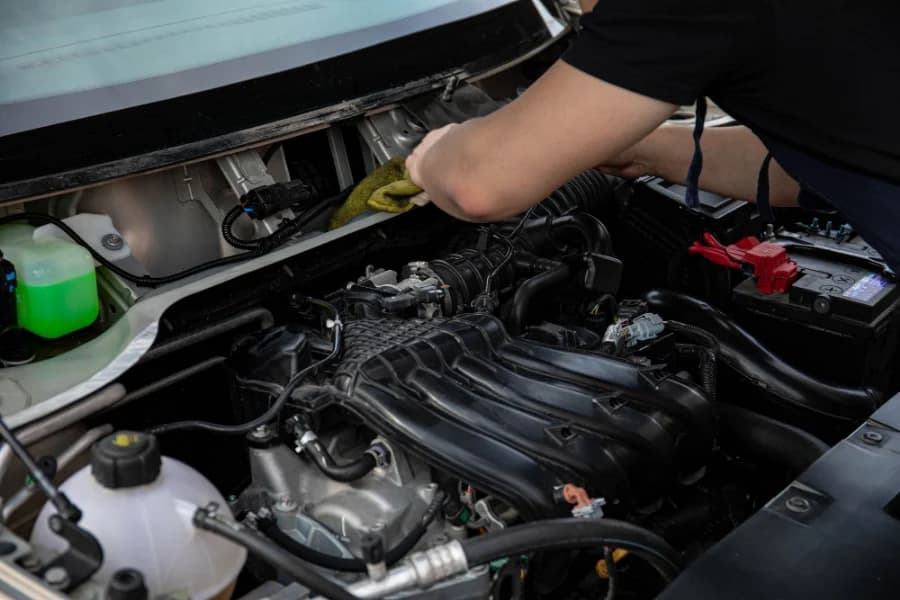Un bras tendu au-dessus d'un moteur ouvert, un chiffon à la main